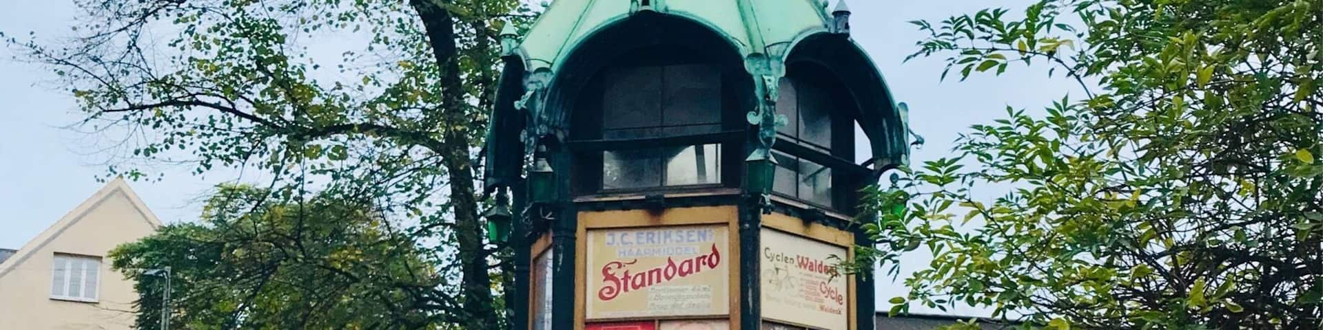 A green clock tower with advertisements and a bicycle parked nearby.