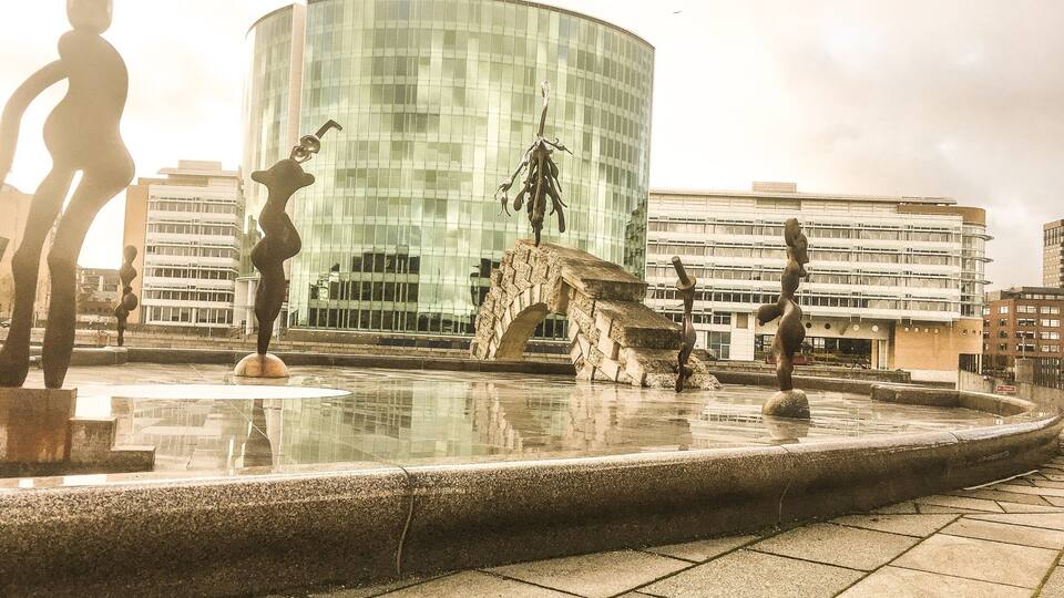 Un jardín de esculturas con figuras abstractas y un edificio moderno de vidrio al fondo.