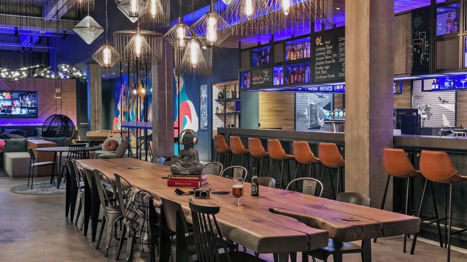 A modern bar with a wooden table, black chairs, and hanging light fixtures.