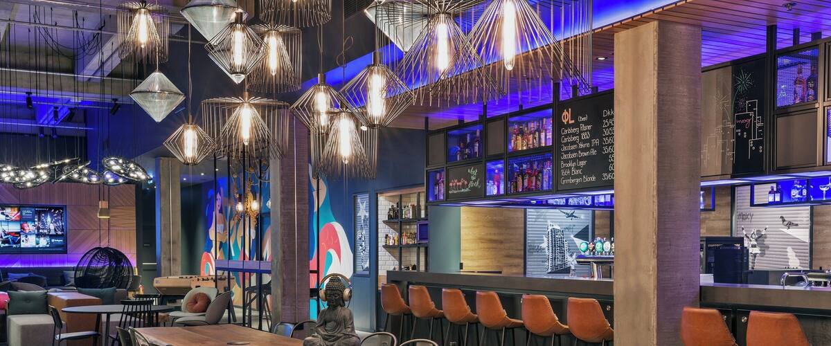A modern bar with a wooden table, black chairs, and hanging light fixtures.