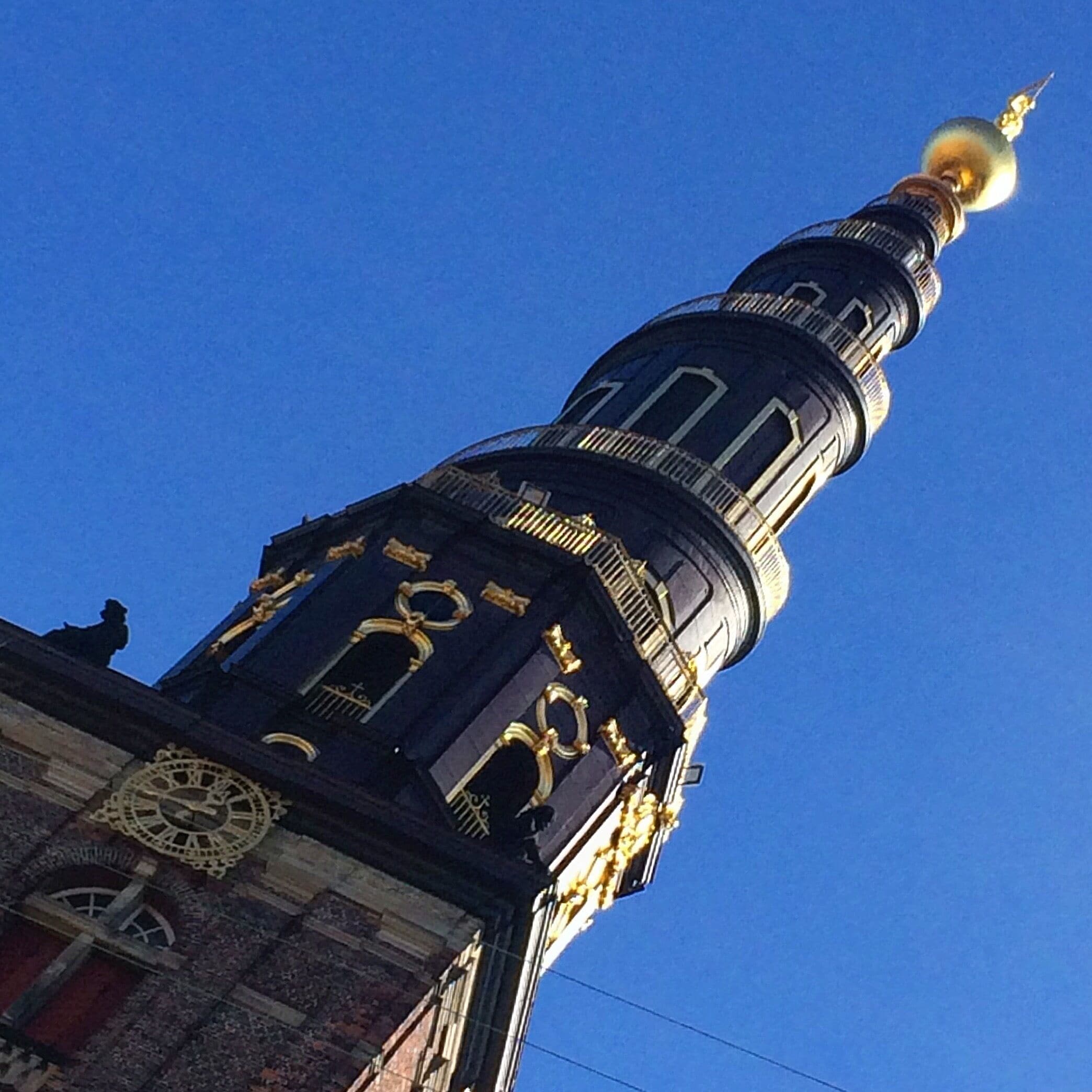 A tower with a clock and a golden spire against a clear blue sky.