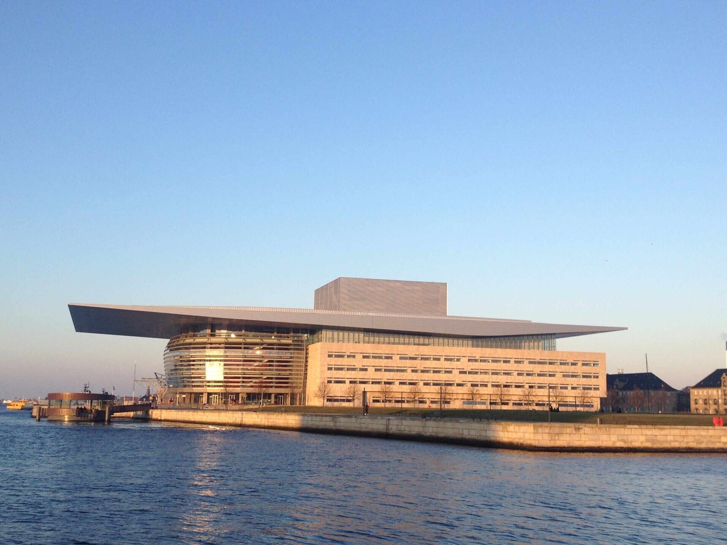 A modern building with a flat roof and a large overhang, situated by a body of water.