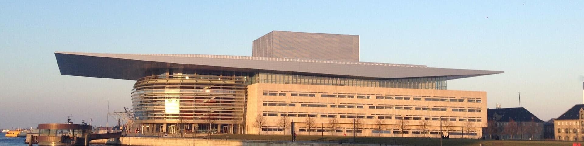 A modern building with a flat roof and a large overhang, situated by a body of water.