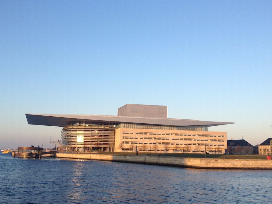 Een modern gebouw met een plat dak en een brede uitbouw, gelegen aan een waterpartij.