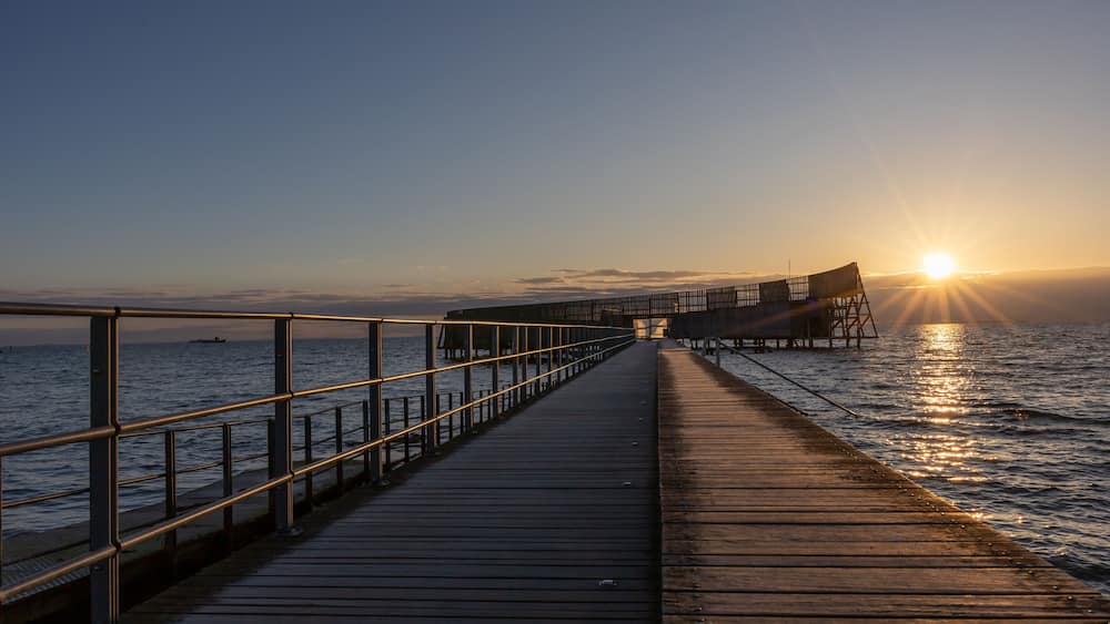 Une jetée en bois s’étendant sur des eaux calmes au coucher du soleil.