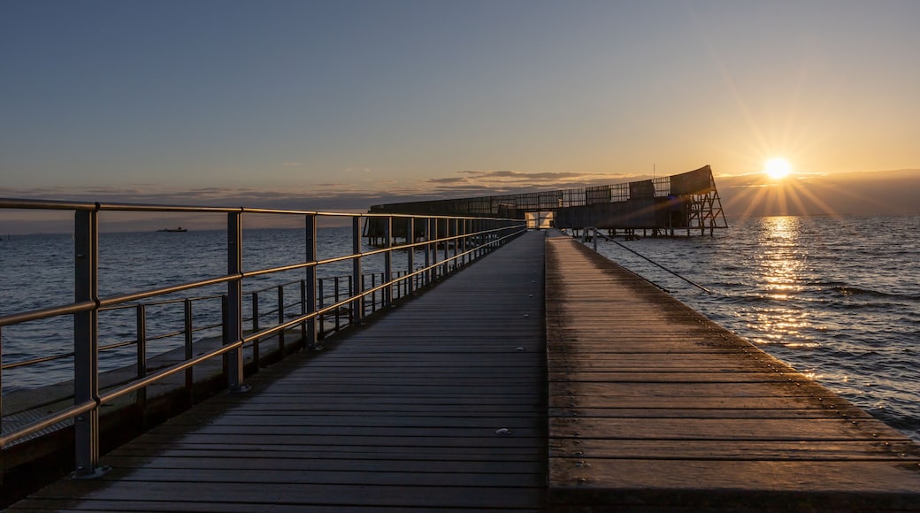 A wooden pier extending into calm waters at sunset.