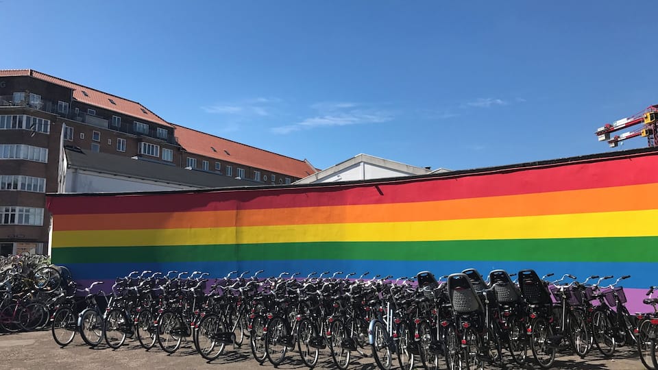 A rainbow flag mural with a row of bicycles in front.