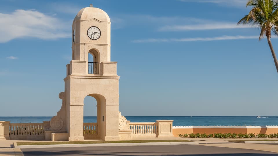 A clock tower with a clear view of the ocean and a palm tree.
