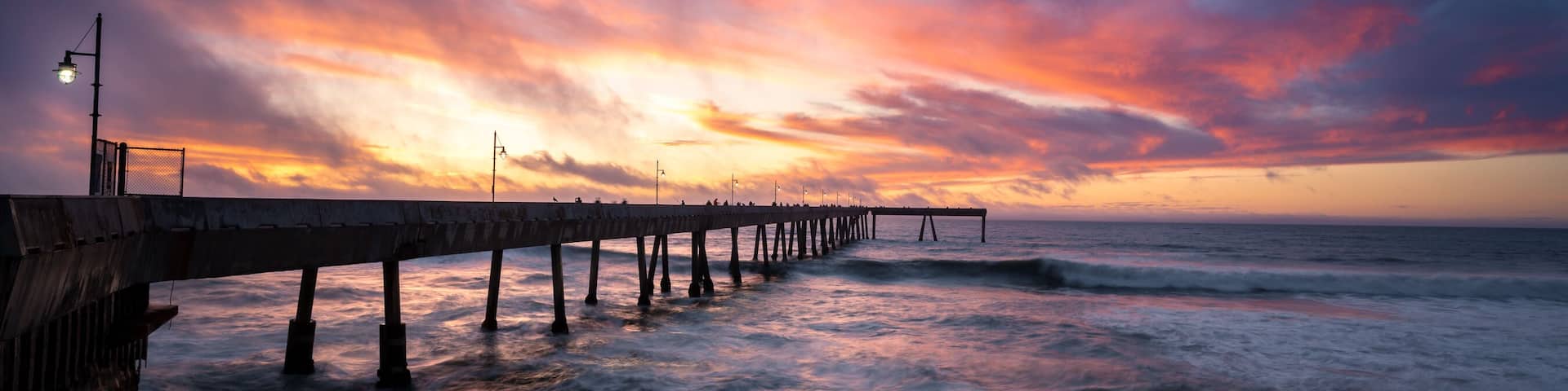 A pier extending into the ocean with a sunset in the background.