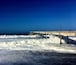 A pier extending into the ocean with waves crashing against it.