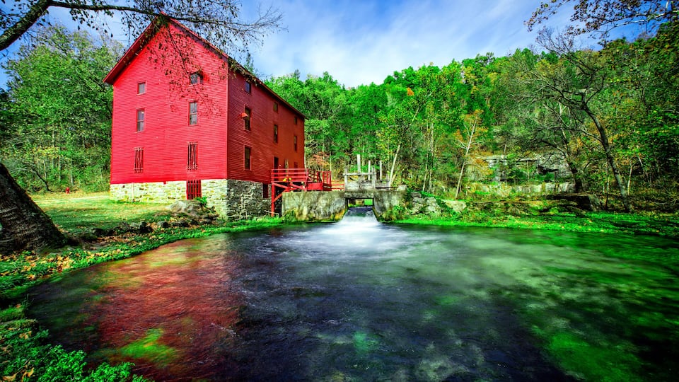 A red barn by a river with a stone bridge.