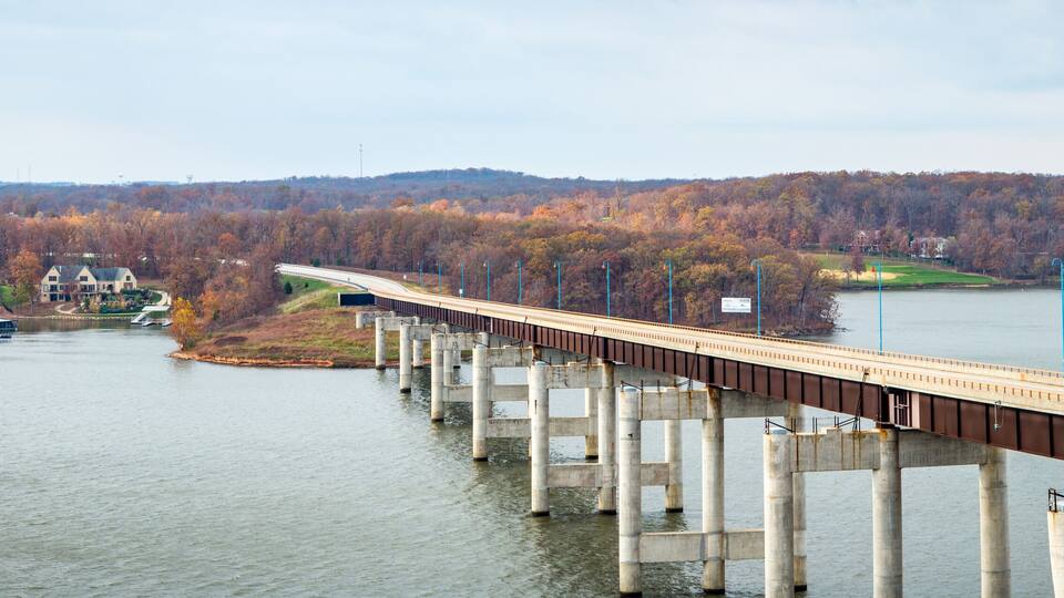 A bridge over a river with autumn foliage in the background.