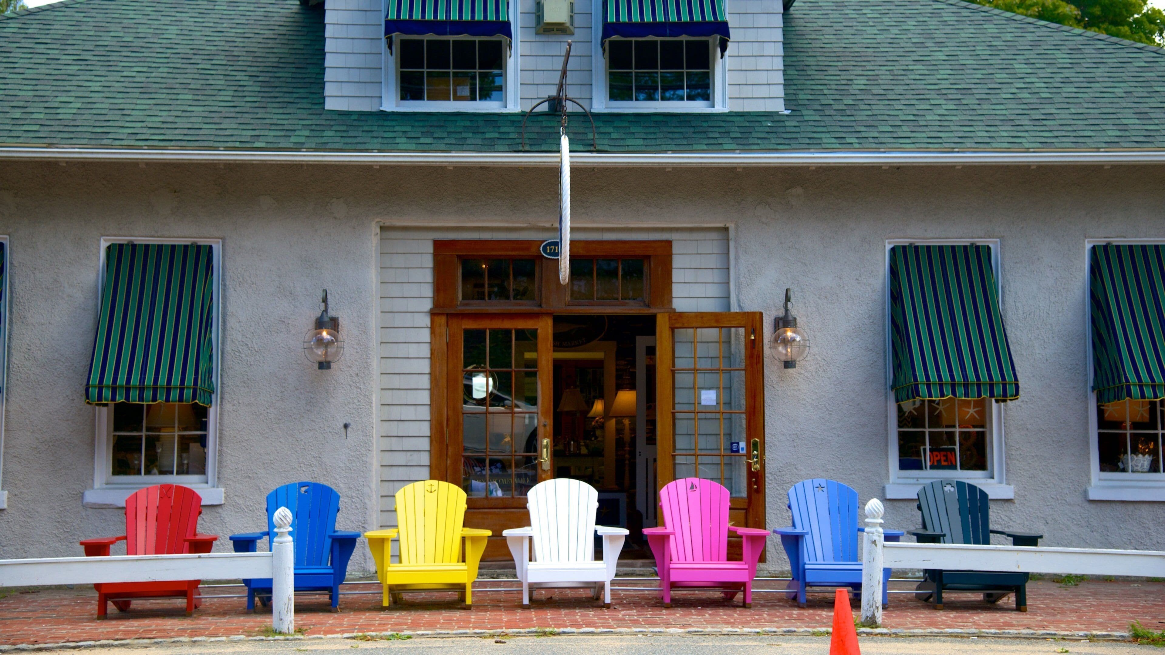 A building with a green roof, white siding, and a wooden door. There are colorful Adirondack chairs in front of the building.