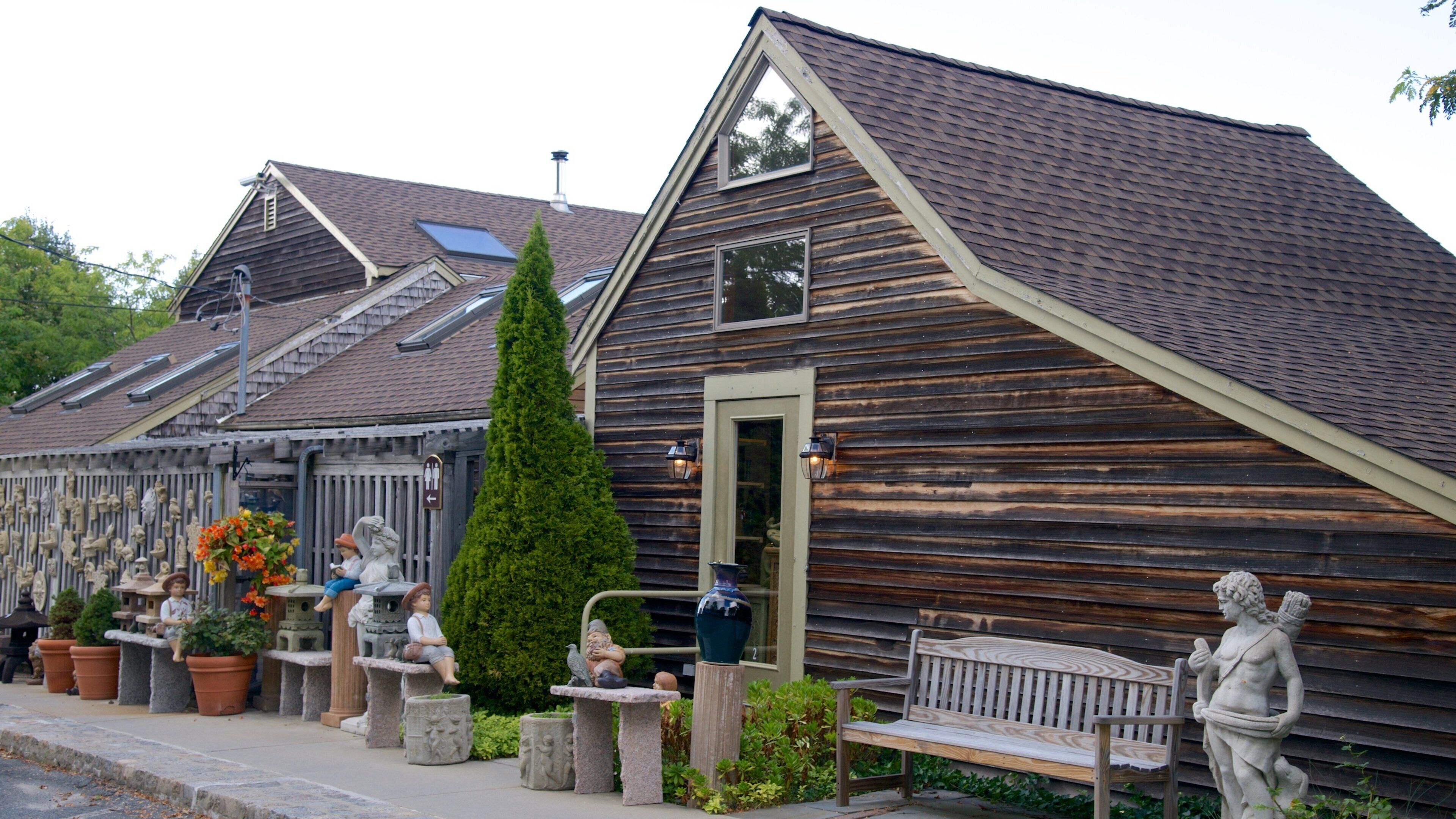 A wooden building with a sloped roof, stone benches, and statues.