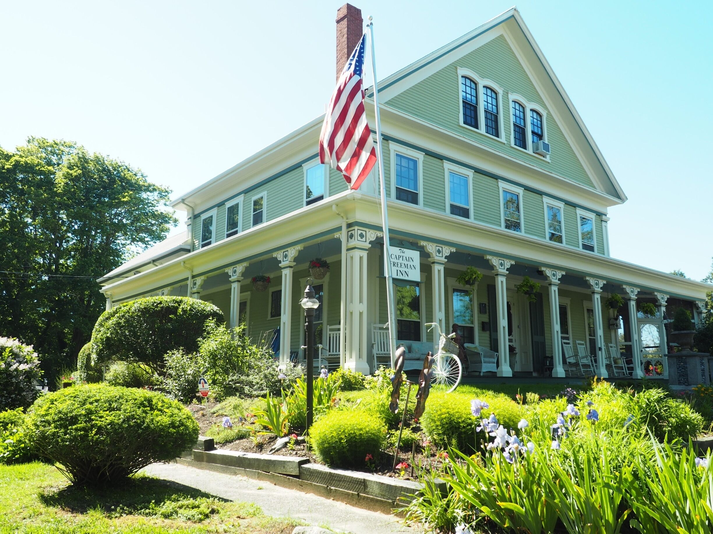 A large, two-story house with a green facade and white trim, featuring a porch with white columns and a sign that reads "The Captain Freeman Inn."
