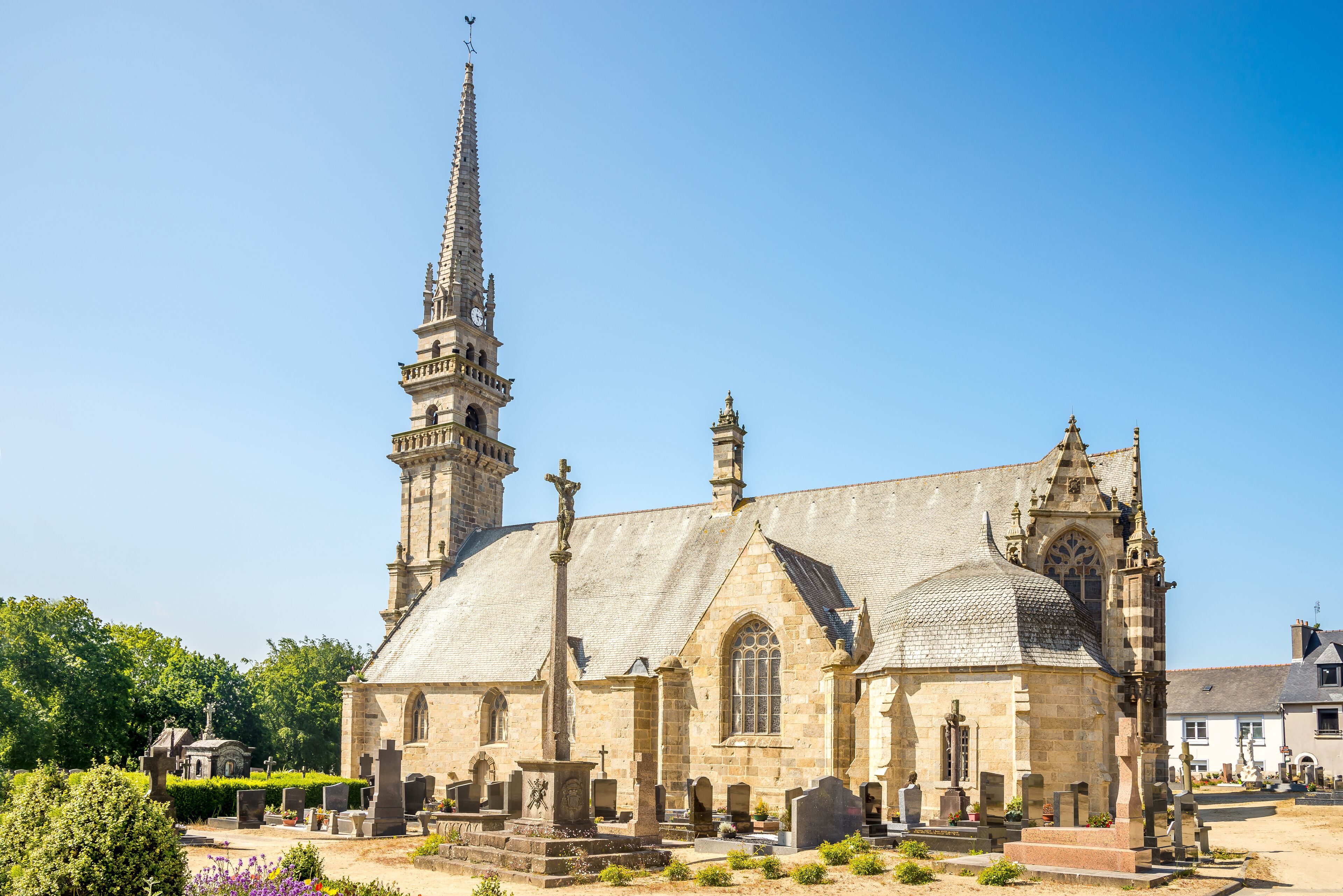 A historic church with a tall spire, a large rose window, and a cemetery in front.