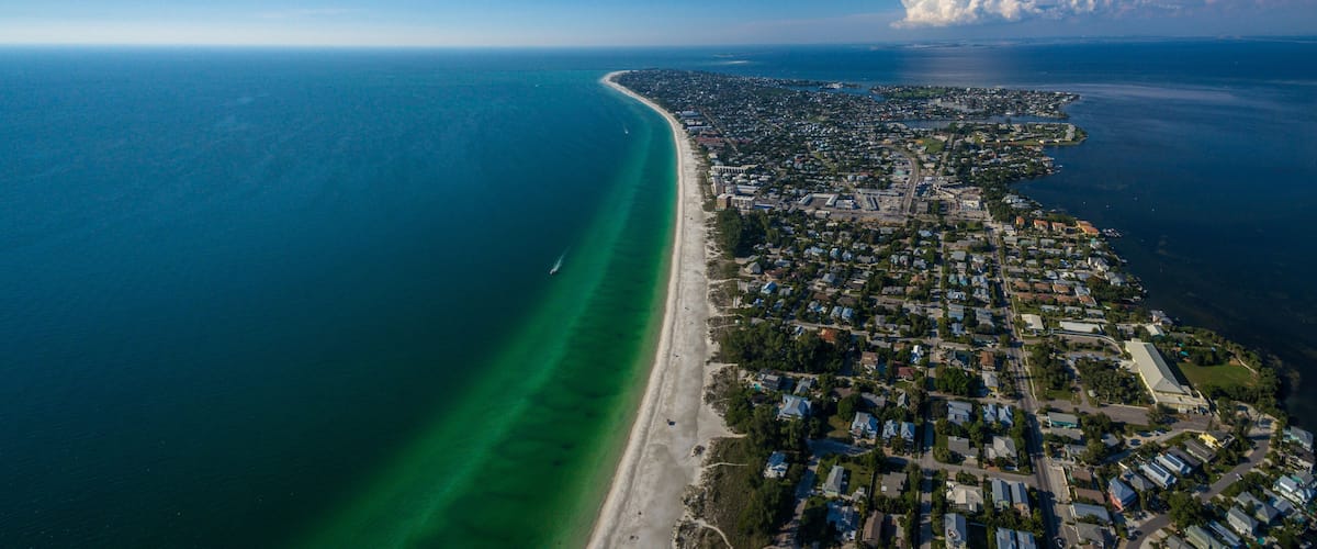 An aerial view of a coastal city with a long beachfront, dense residential area, and a large cloud formation.