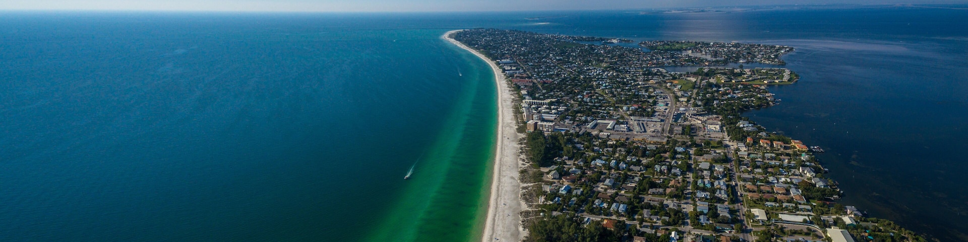 An aerial view of a coastal city with a long beachfront, dense residential area, and a large cloud formation.