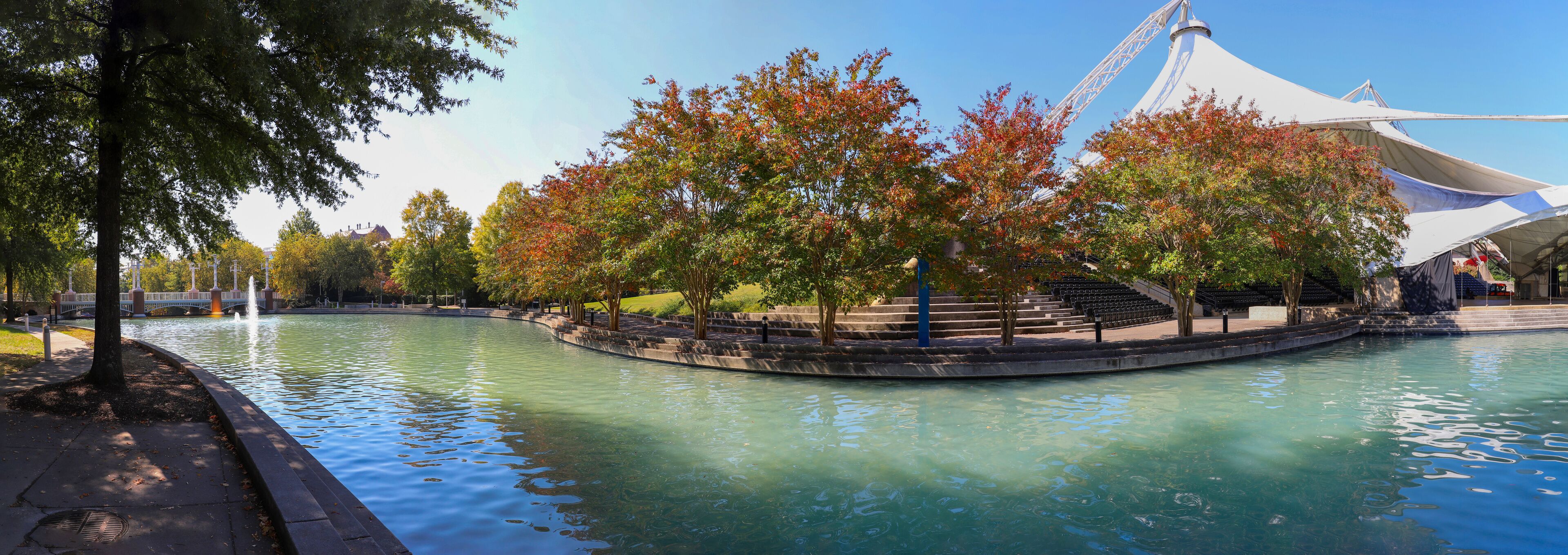 a stunning autumn landscape at World's Fair Park with a pool with blue water surrounded by red and yellow autumn trees and lush green trees and plants with a gorgeous blue sky in Knoxville