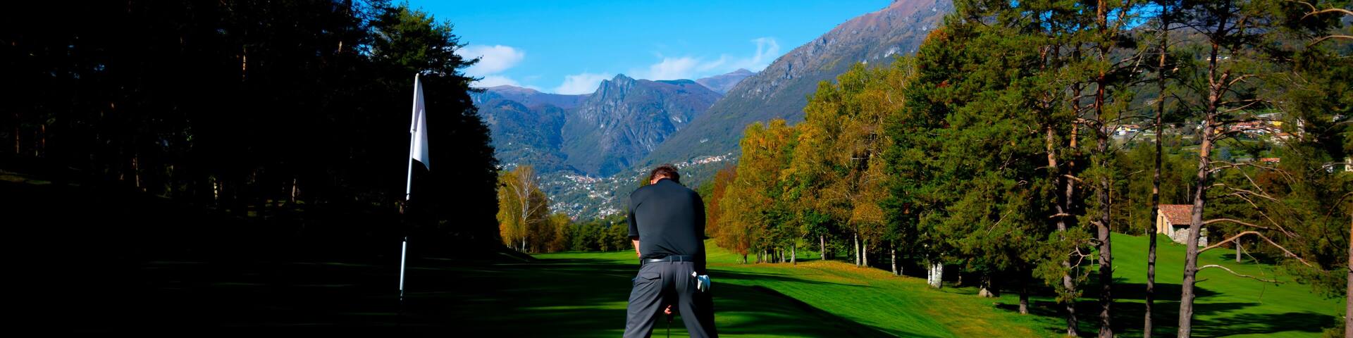 A golfer on a green with mountains in the background.