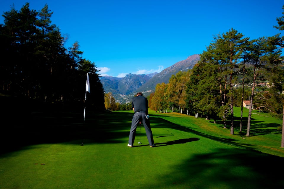 A golfer on a green with mountains in the background.