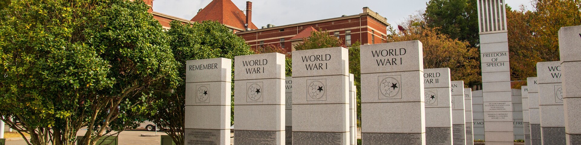 a gorgeous autumn landscape at East Tennessee Veterans Memorial in World's Fair Park with stone slabs surrounded by autumn colored trees and lush green trees and cloudy sky in Knoxville Tennessee USA