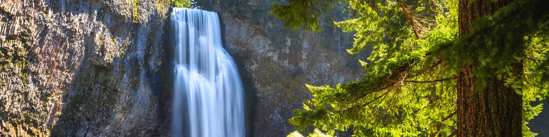 A waterfall cascading down a rocky cliff surrounded by evergreen trees.