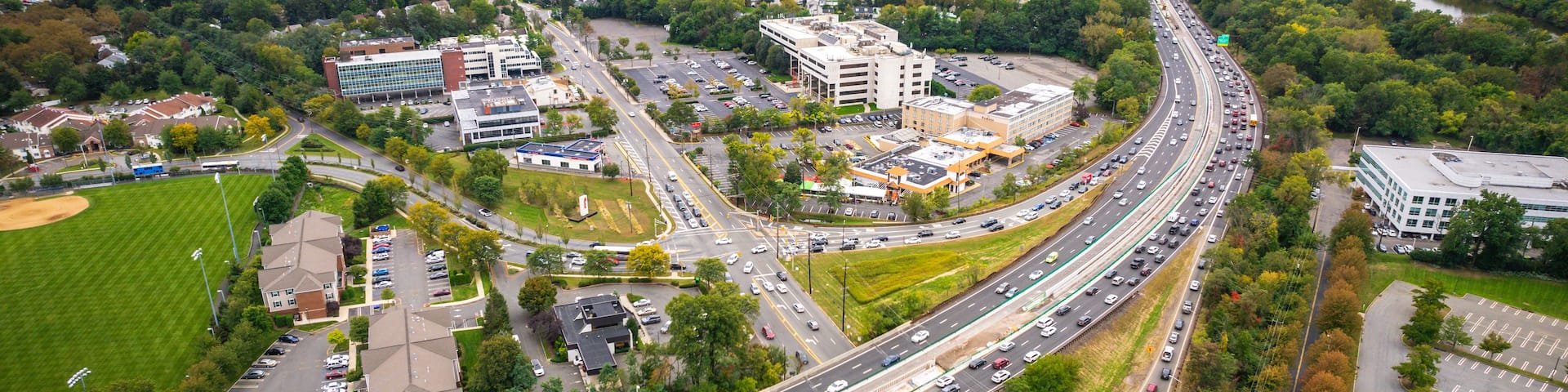 A multi-level highway interchange with surrounding residential areas and a distant city skyline.