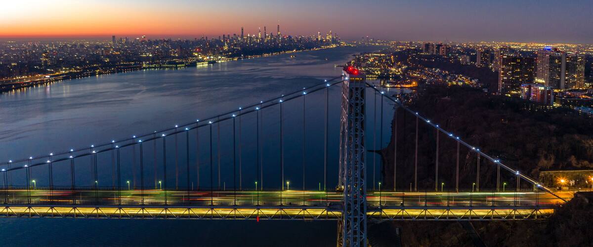 A suspension bridge at dusk with city lights in the background.