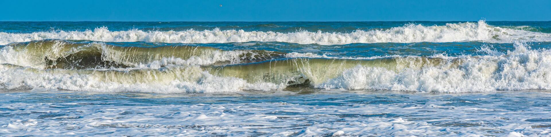 Waves crashing onto a sandy beach under a clear blue sky.