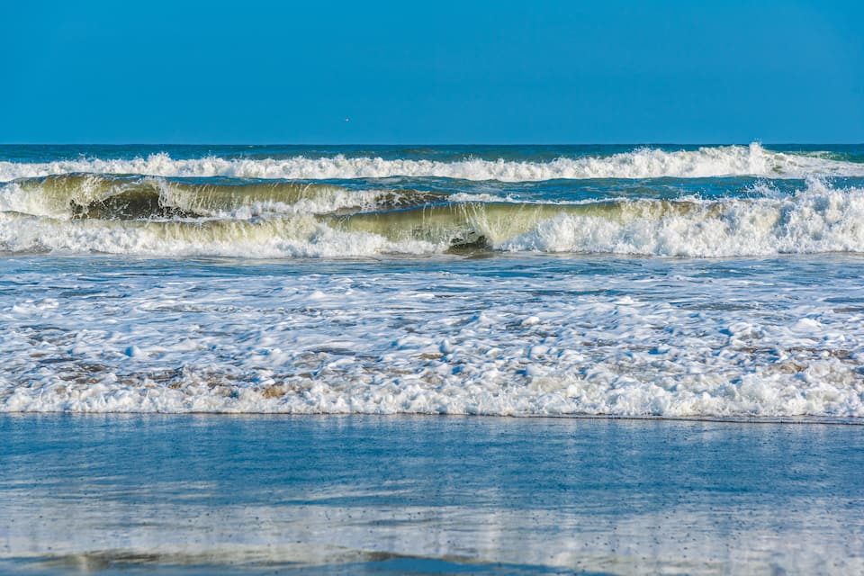 Waves crashing onto a sandy beach under a clear blue sky.