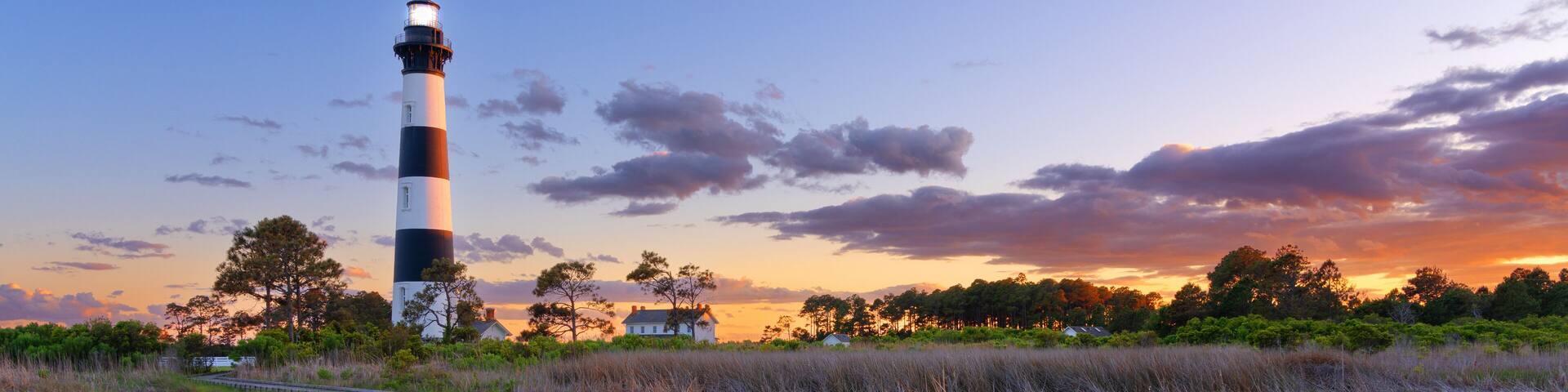 A lighthouse, a wooden boardwalk, and a sunset over a marshy landscape.
