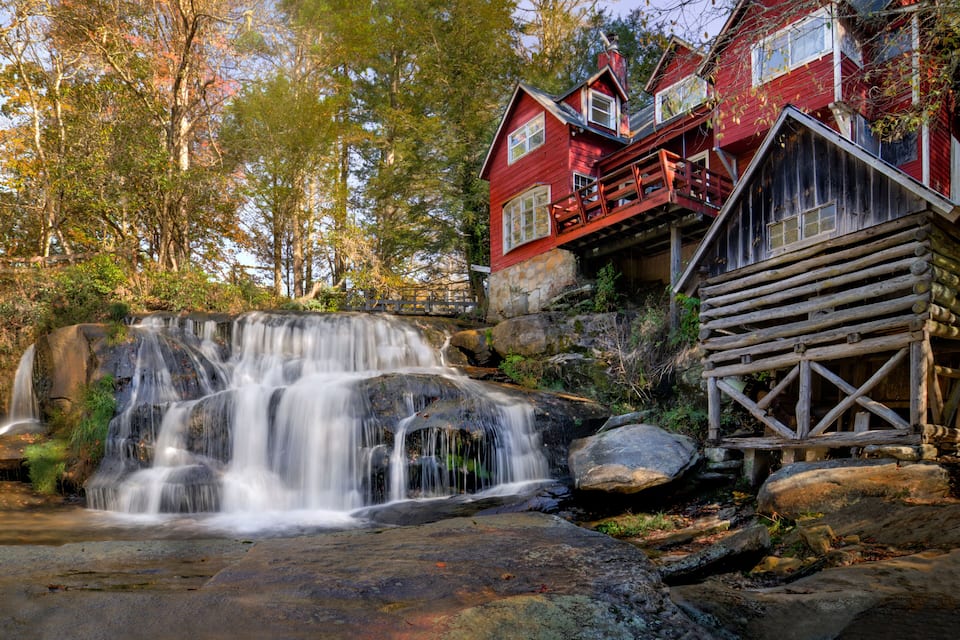 A red log cabin with a waterfall in front.