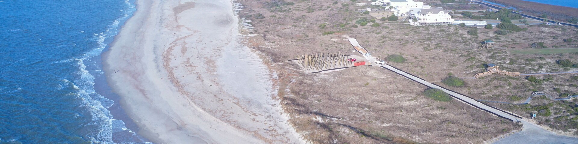Aerial view from over the water of Oak Island point looking toward Holden Beach. The waves are crashing onto the beach. View of the tip of the Island.