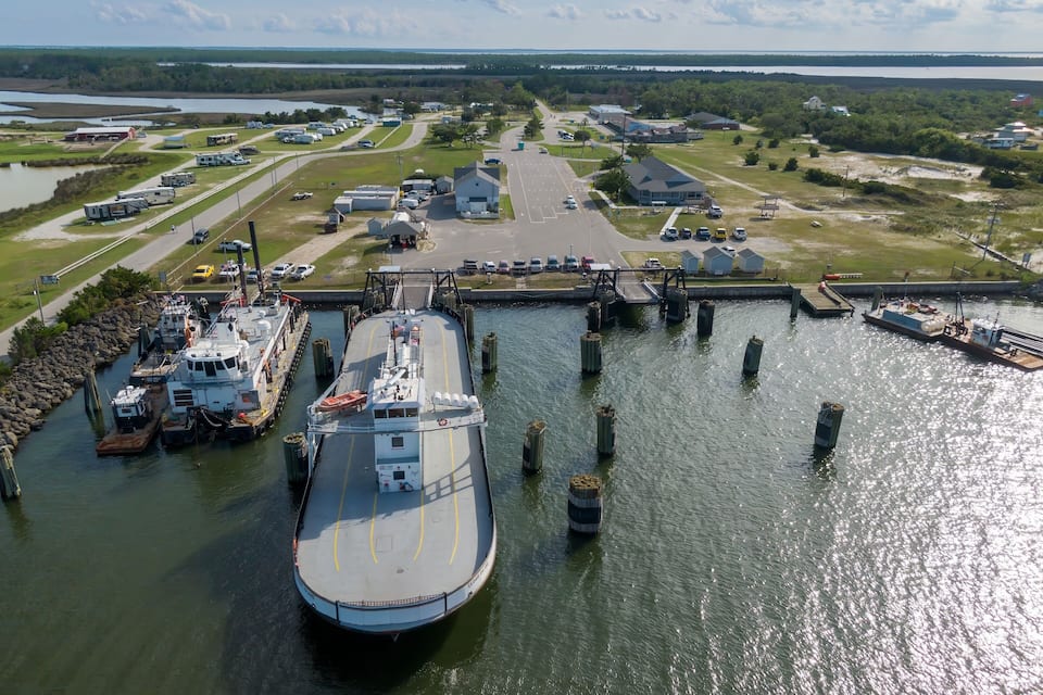A large ferry docked at a pier with a marina and buildings in the background.