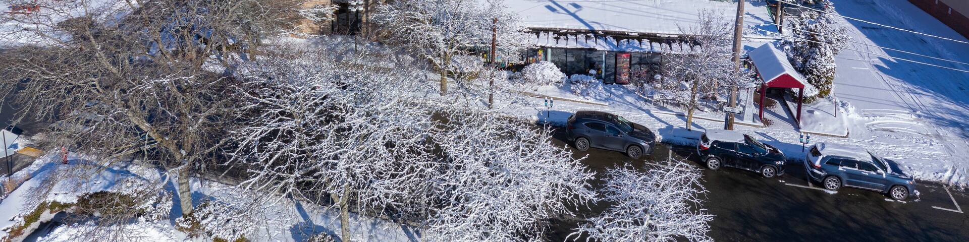 A historic building with a tower and steeply pitched roof, surrounded by snow-covered trees and parked cars.