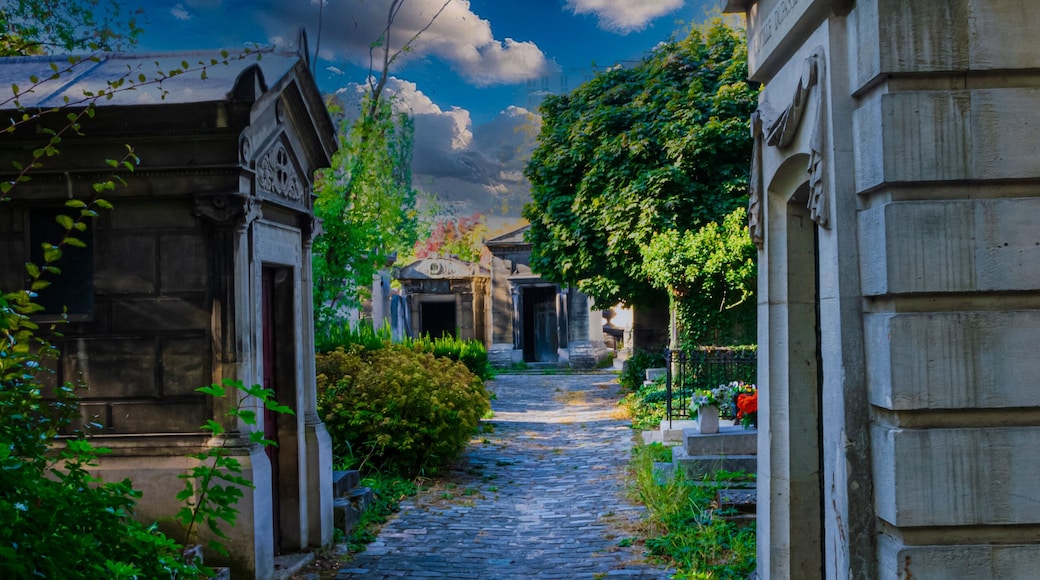 A cobblestone pathway flanked by stone buildings and lush greenery under a partly cloudy sky.