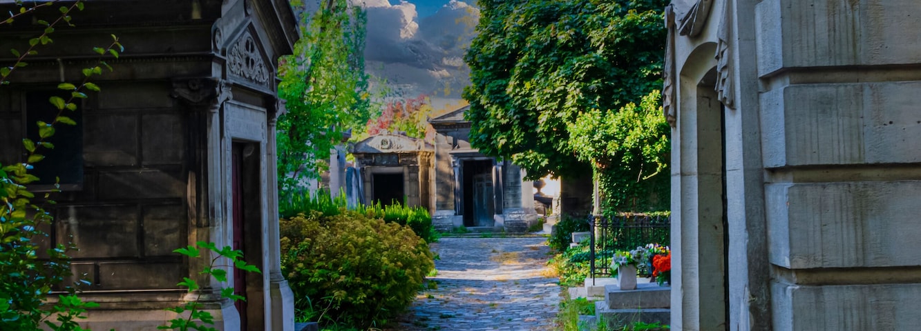 Uma rua de paralelepípedos ladeada por edifícios de pedra e vegetação exuberante sob um céu parcialmente nublado.