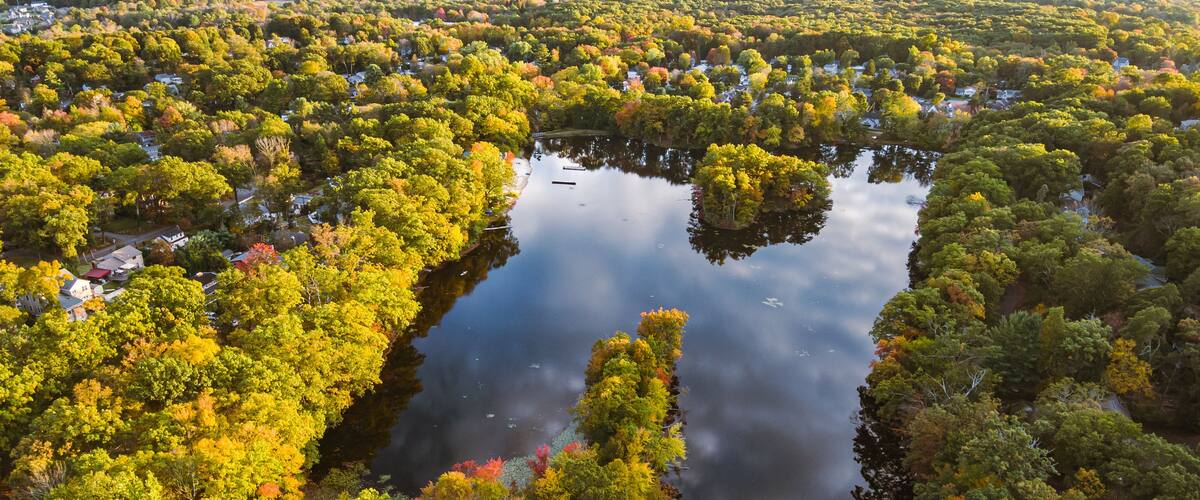 An aerial view of a lake surrounded by dense forest with autumn foliage.