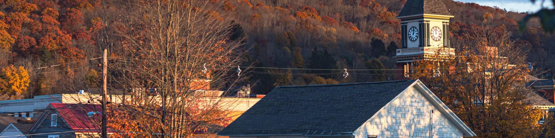 A town with a prominent clock tower, surrounded by autumn-colored trees and houses.