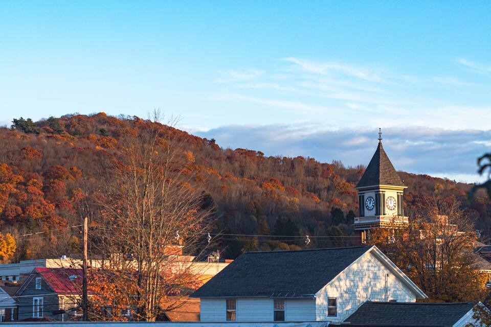 A town with a prominent clock tower, surrounded by autumn-colored trees and houses.