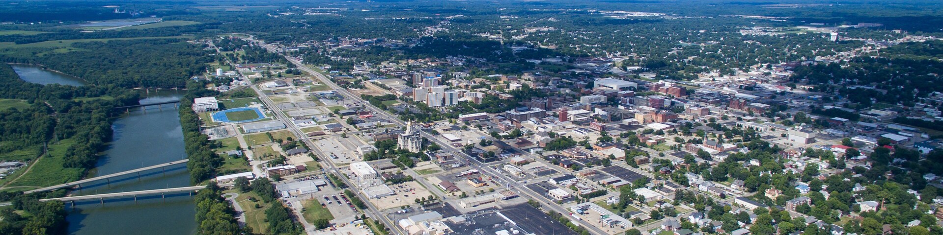 An aerial view of a city with a river, industrial area, and green spaces.