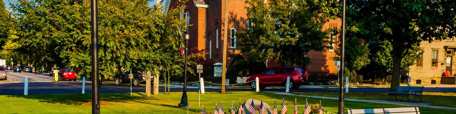 A park with a bench, a clock tower, and a flag display.