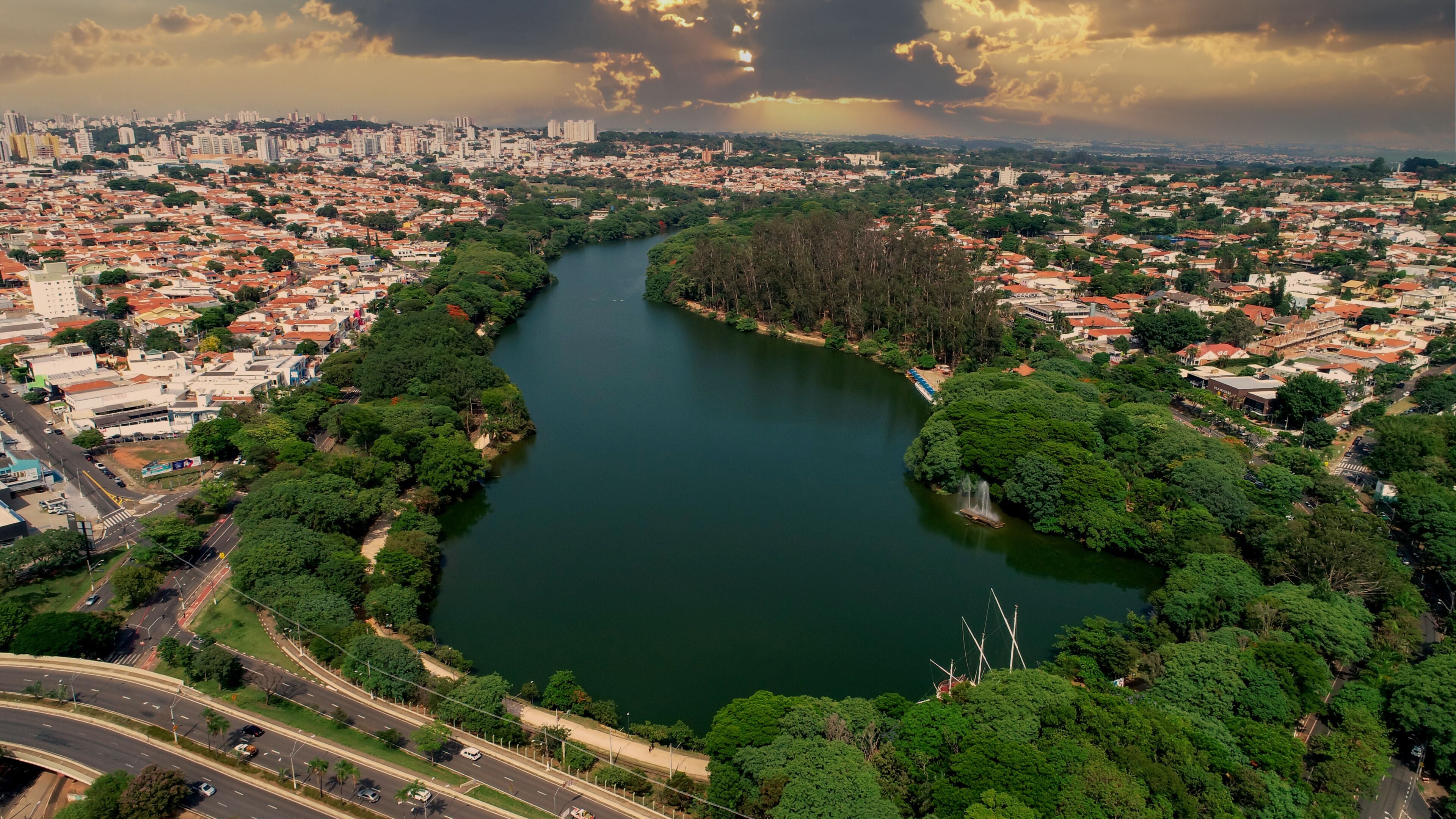 A river winding through a city with dense greenery and a distant urban skyline.