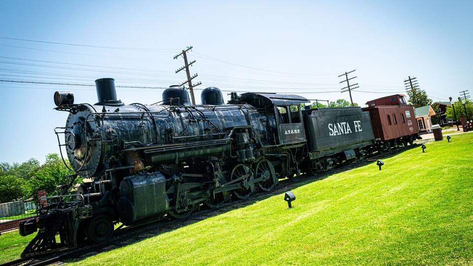 A vintage steam locomotive named Santa Fe on display in a grassy area with a clear blue sky.