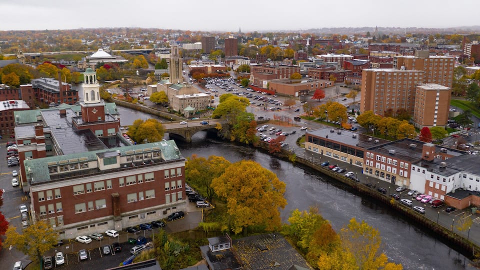 A cityscape with a prominent church tower, a river, and autumn-colored trees.