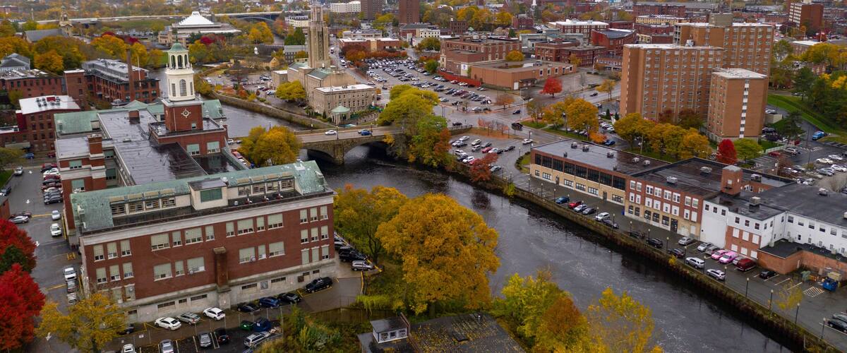A cityscape with a prominent church tower, a river, and autumn-colored trees.