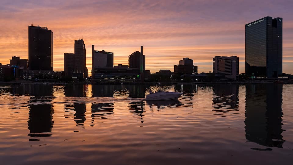 A city skyline at sunset with a boat on the water.