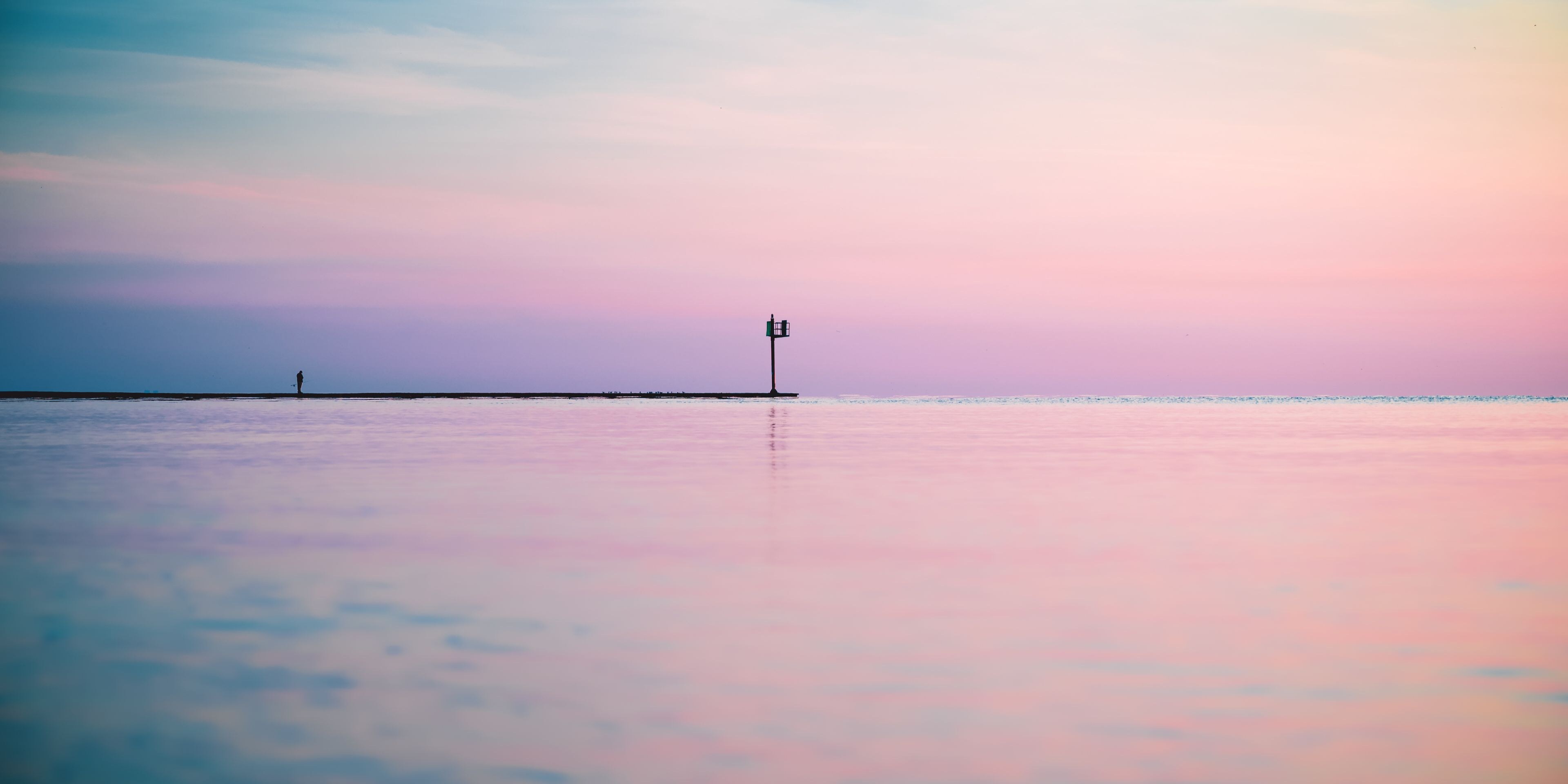 A beach with a lighthouse and a person walking.