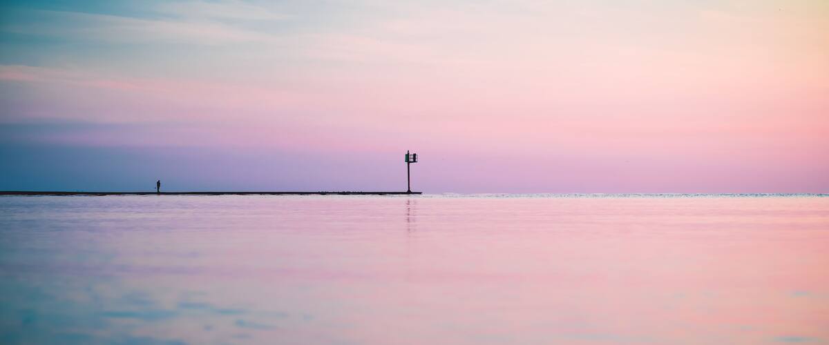 A beach with a lighthouse and a person walking.
